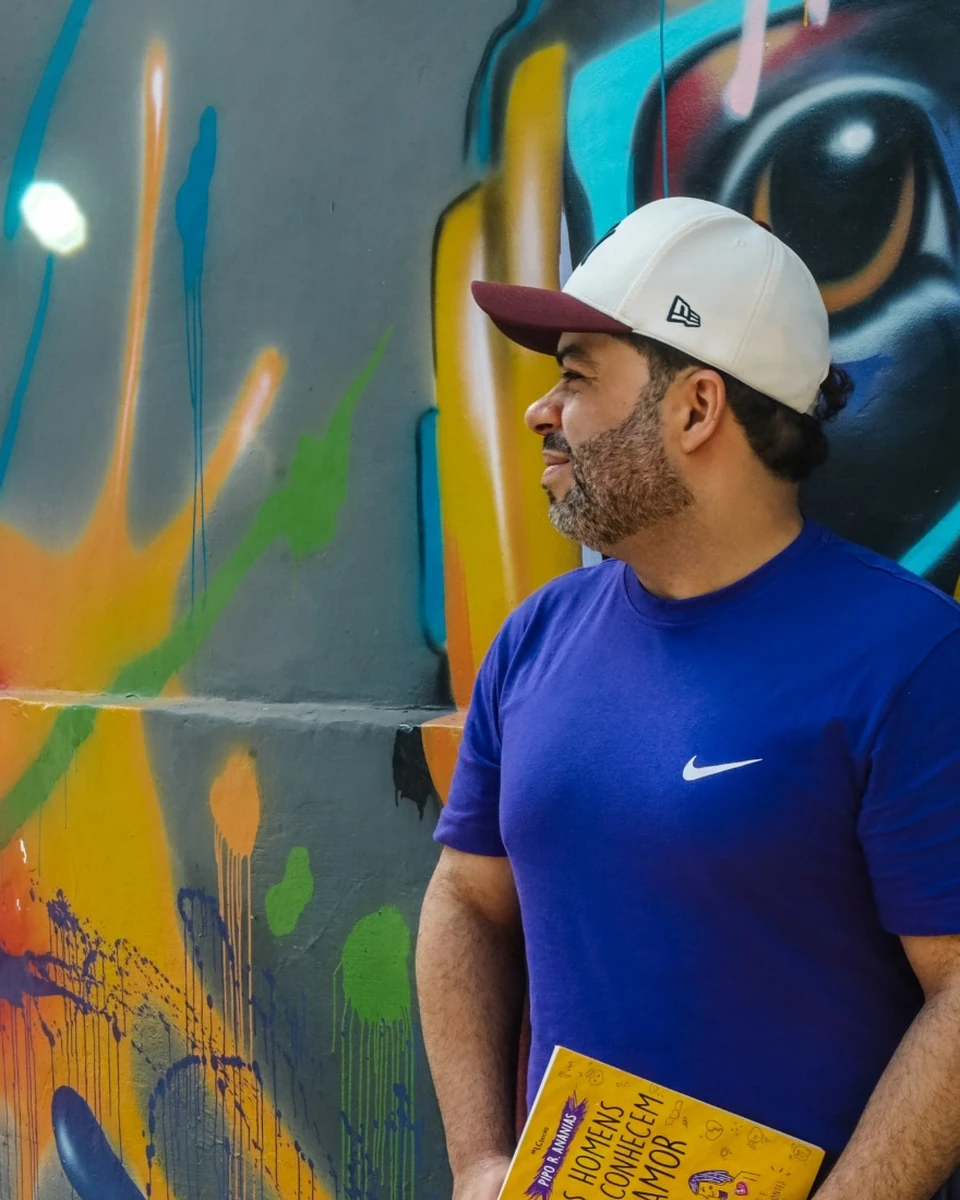 Pipo R. Ananias com o livro Os Homens Não Conhecem o Amor diante de um grafite